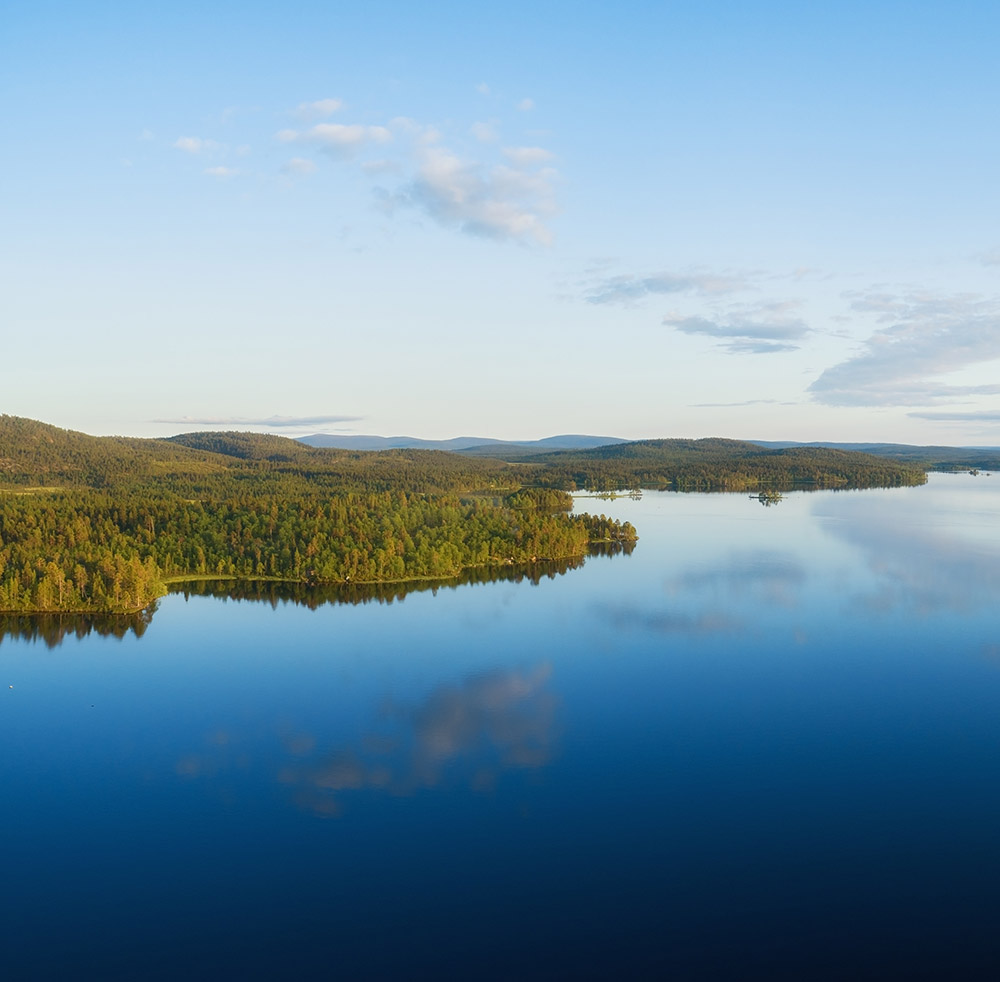 ilmakuva suomalaisesta suuresta tyynestä järvestä kesällä. Taustalla näkyy suuria metsiä ja sininen taivas.