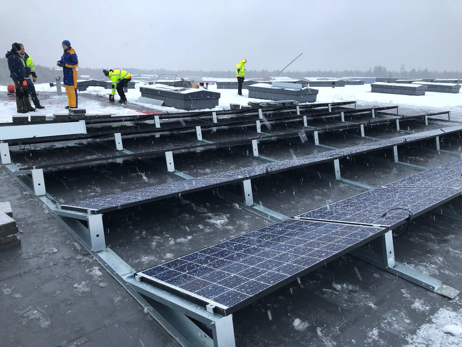 aurinkopaneelien asennusta lumisella katolla useiden miesten voimin