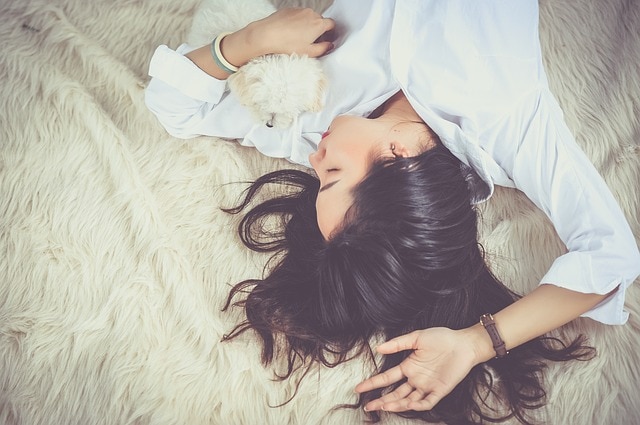 tummahiuksinen nainen vaaleassa paidassa makaa karvamatolla