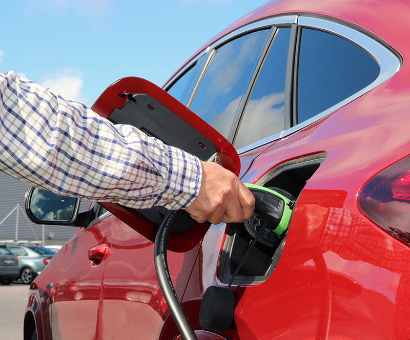 Sähköauton latauslaitteet, maahantuoja Scanoffice Solar Oy, miehen käsi laittaa punaista sähköautoa lataukseen.