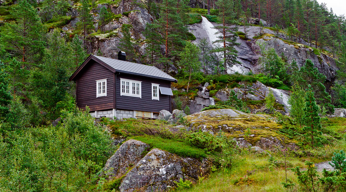 Pohjoismaalainen mökki vihreän ja kallioisen metsän keskellä.
