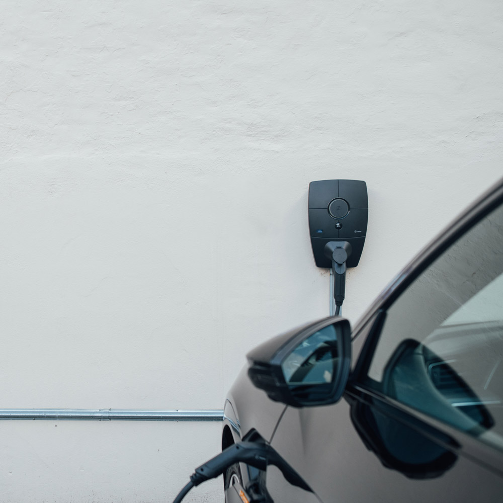 Kaksi seinälle asennettua Zaptec-latausasemaa taloyhtiön parkkipaikalla, yksi sähköauto latauksessa. Tämä kuvastaa taloyhtiön ratkaisuja kustannusten jakamisessa latauspisteiden asennuksen jälkeen.