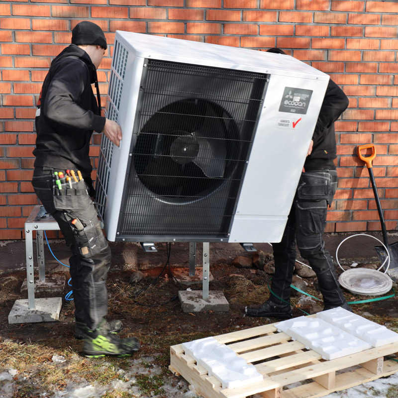 Kaksi scanofficen asentajaa nostaa Mitsubishi electric ecodan -ilmavesilämpöpumpun ulkoyksikköä asennuspaikkaan.