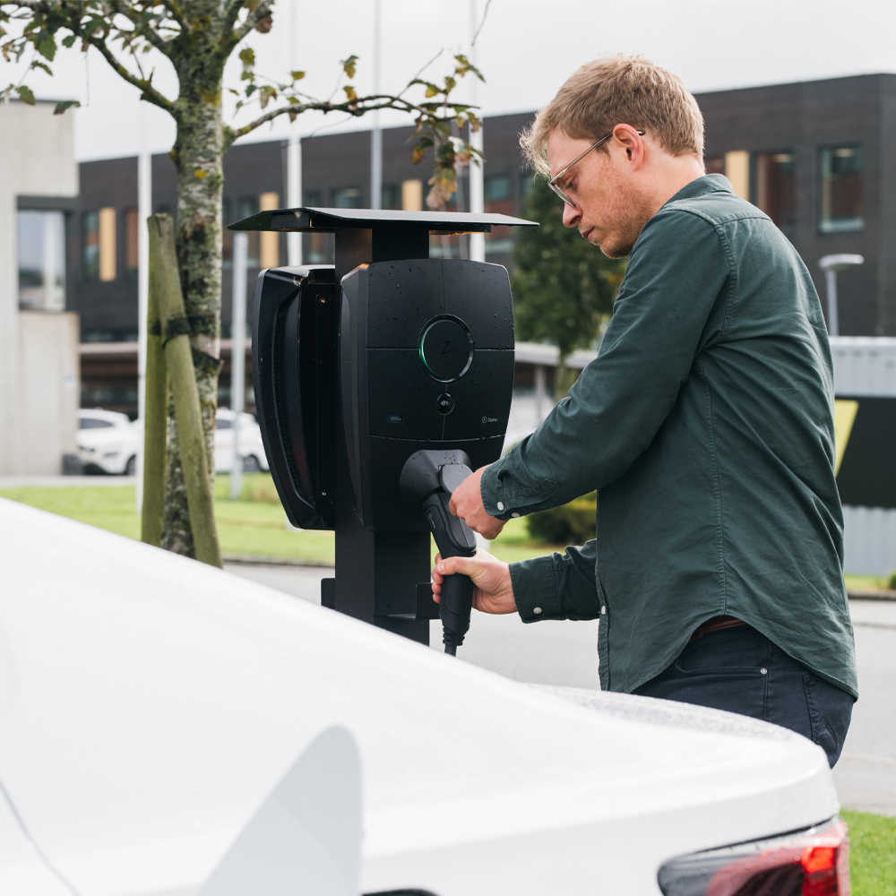 Kaksi sähköautoa latautumassa rinnakkain Zaptec-latausasemilla, kuvastaa kahden sähköauton lataamista samanaikaisesti. Mies on asentamassa latauspistoketta latausasemaan.