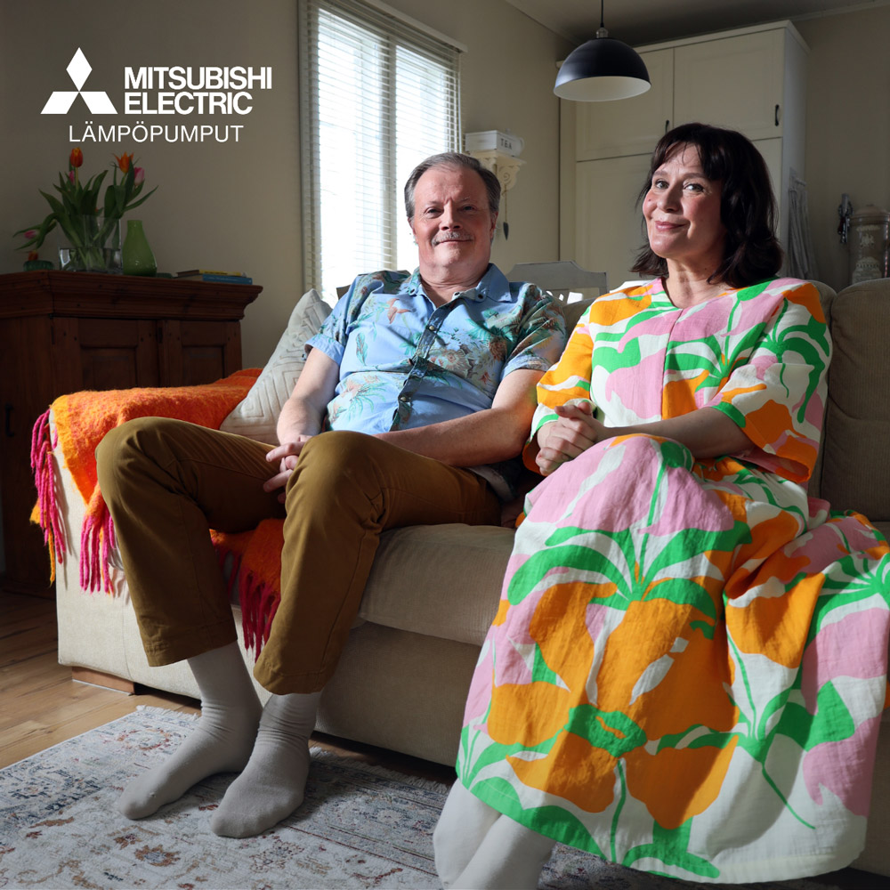 Pumppu-ukko ja hänen vaimonsa istuvat sohvalla ja katsovat kameraan. Molemmilla on päällään tavanomaiset vaatteet. Yläkulmassa on Mitsubishi Electric Lämpöpumput -logo.